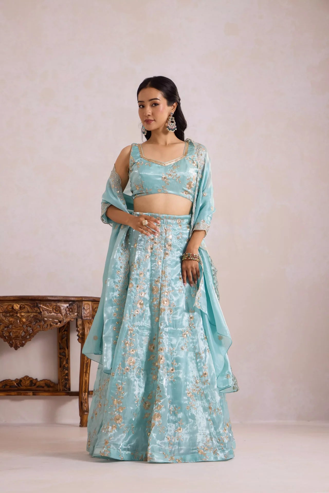 Woman wearing a light blue traditional outfit with gold embroidery against a plain background